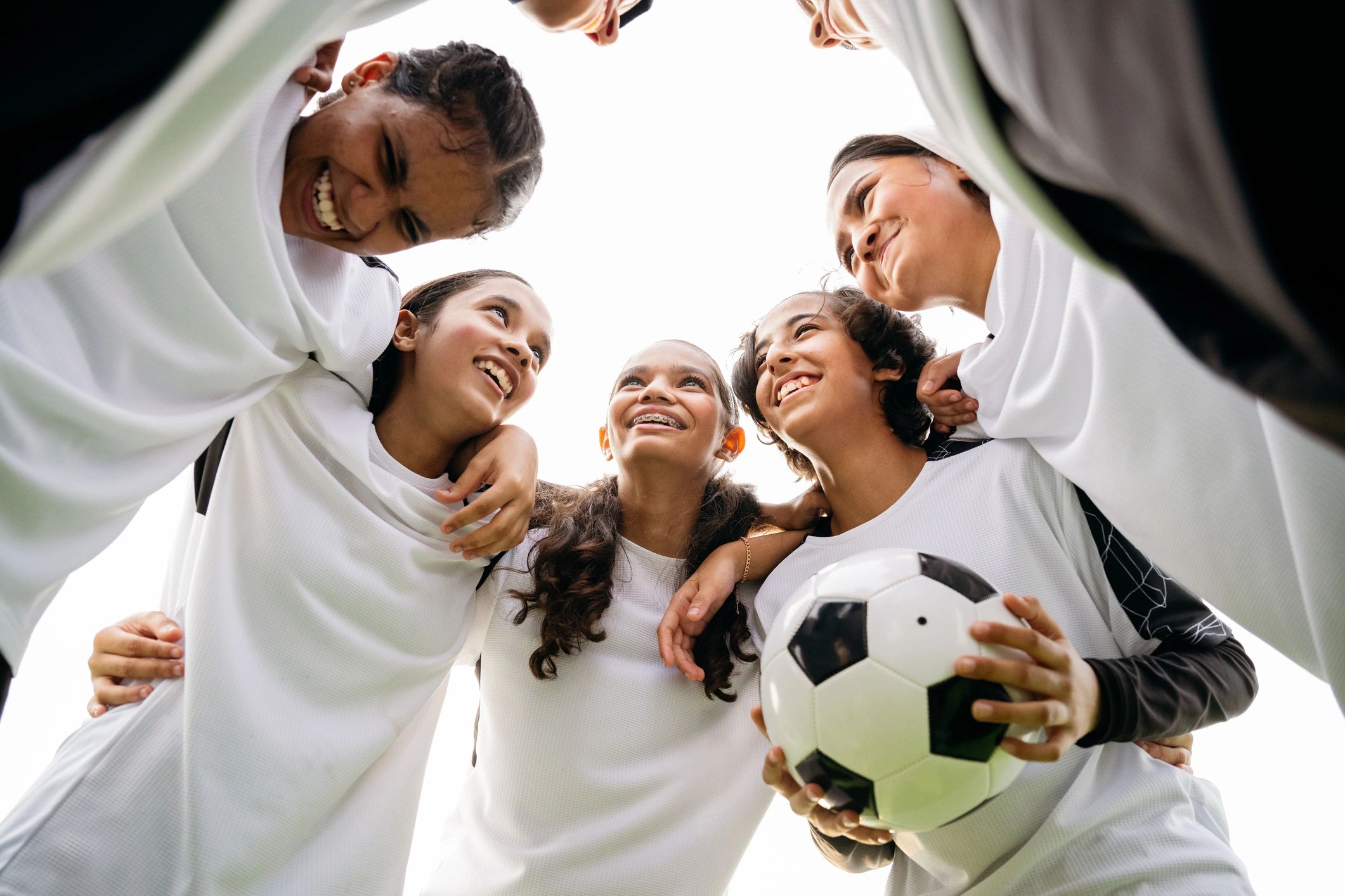 Female soccer players standing in huddle with ball